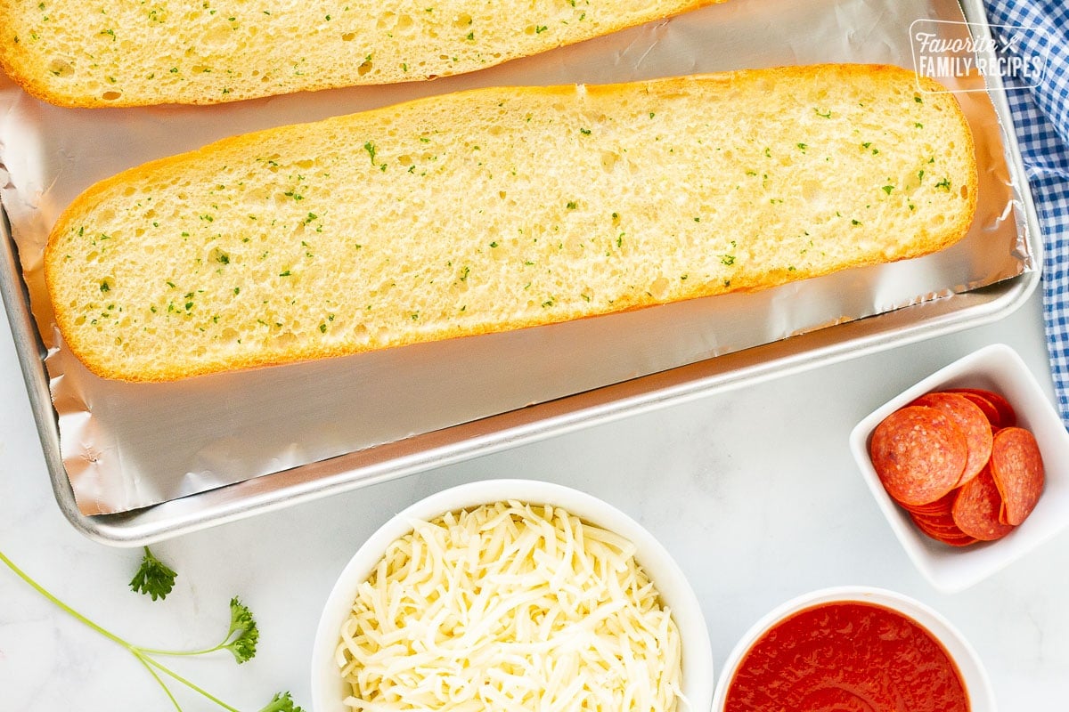 Golden toasted butter French bread halves for pizza. Pepperoni, cheese and sauce on the side.