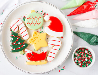 Plate of Christmas Sugar Cookies next to bags of royal icing and sprinkles.