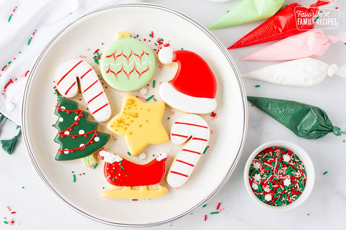 Plate of Christmas Sugar Cookies next to bags of royal icing and sprinkles.