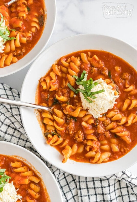 Three bowls of lasagna soup topped with cheese mixture and basil