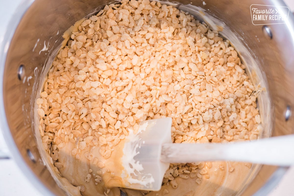 Rice Krispies being added to a marshmallow mixture in a large pot on the stovetop