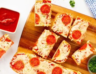 Pieces of French Bread Pizza on a cutting board next to marinara sauce.
