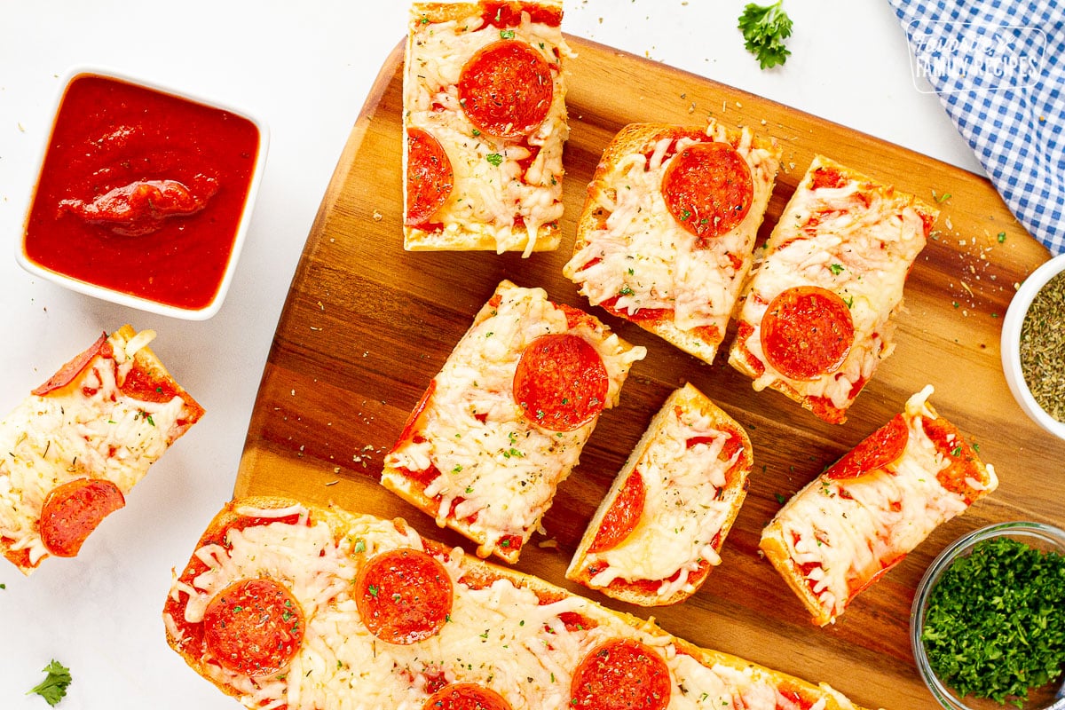 Pieces of French Bread Pizza on a cutting board next to marinara sauce.