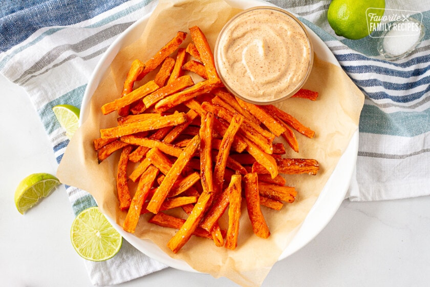 Sweet Potato Fries on a plate with dipping sauce. Limes and salt on the side.