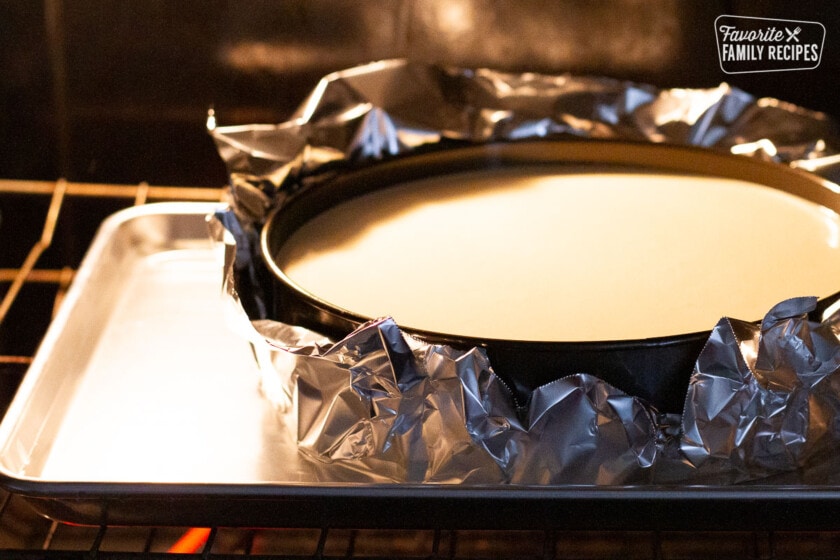 Springform pan wrapped in foil in a water bath in the oven for Raspberry Cheesecake.