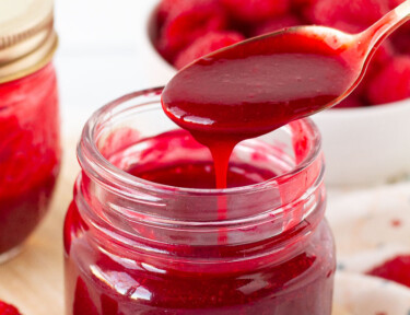 Spoon drizzling Raspberry Sauce into a jar.