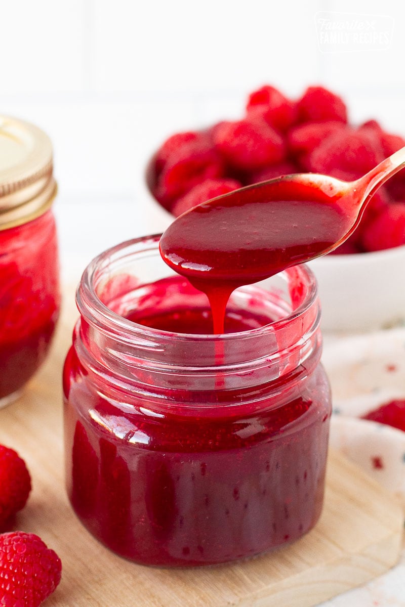 Spoon drizzling raspberry coulis into a jar.
