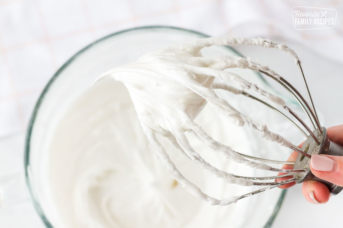 Hand holding a mixing whisk of Royal Icing.