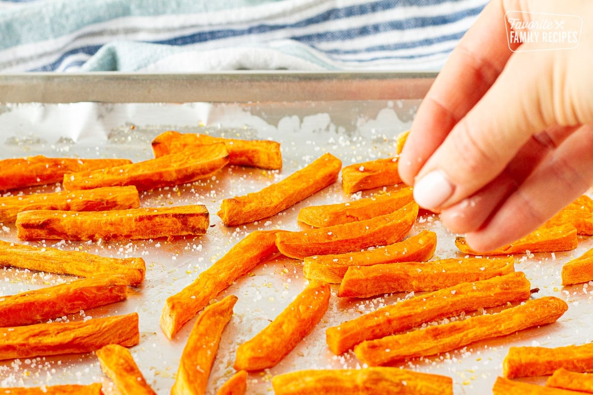 Hand sprinkling salt onto baked Sweet Potato Fries.