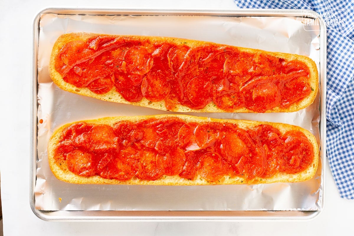 Sauce and pepperoni french bread on a baking sheet.