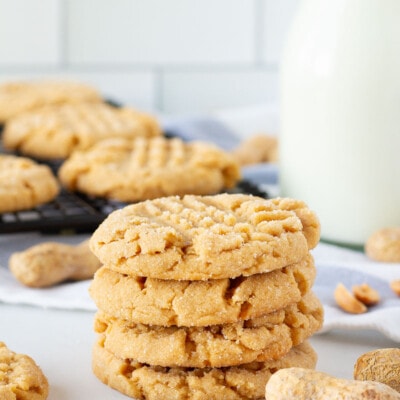 Four Peanut Butter Cookies stacked next to peanuts.