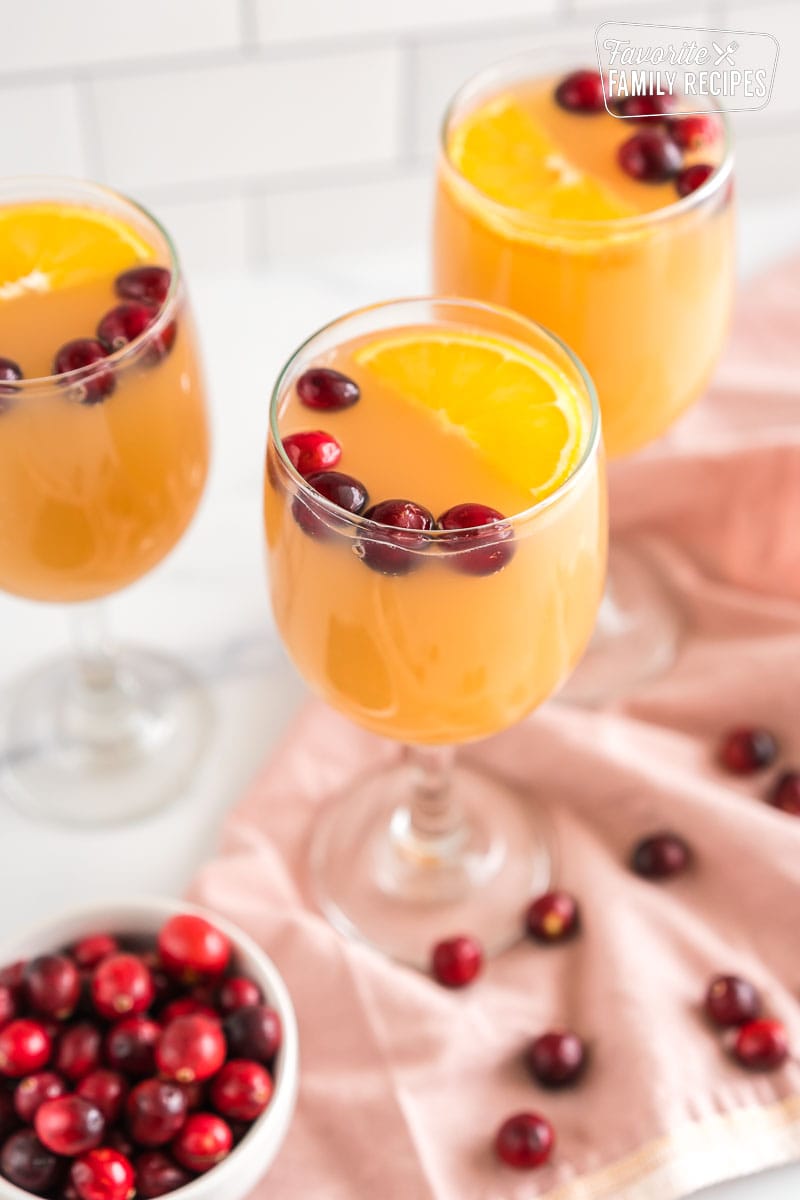 A glass of sparkling cider topped with an orange slice and cranberries