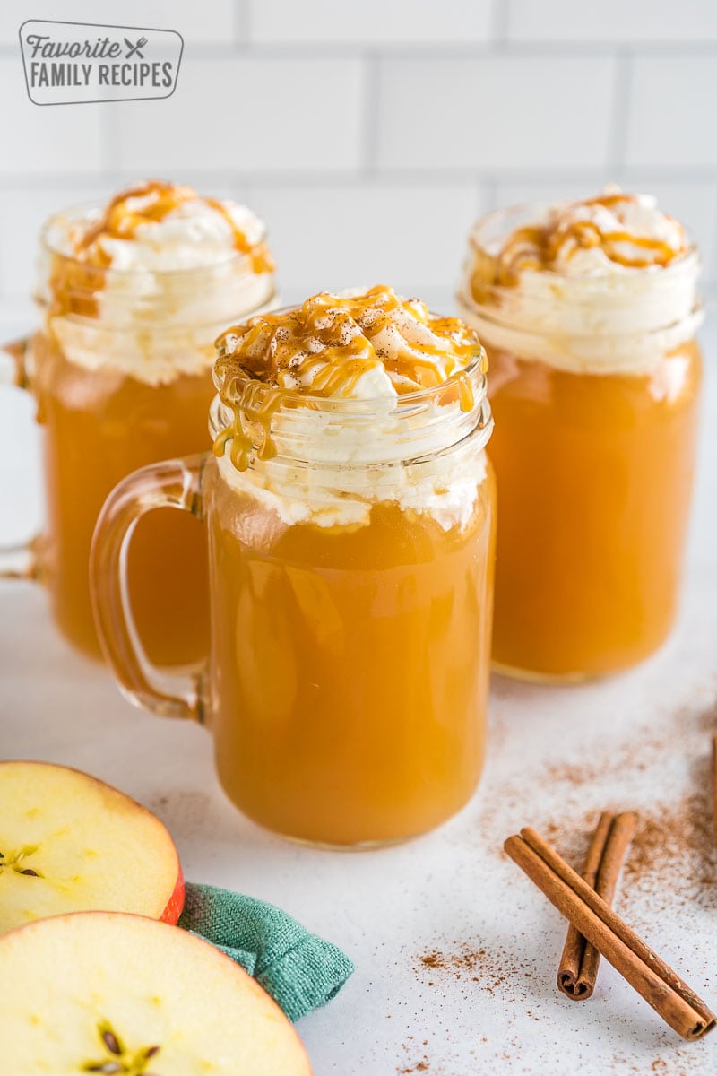 Three mugs of Starbucks Caramel Apple Spice Cider topped with whipped cream and caramel