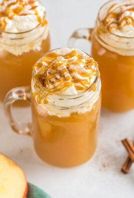 Three mugs of Starbucks Caramel Apple Spice Cider topped with whipped cream and caramel