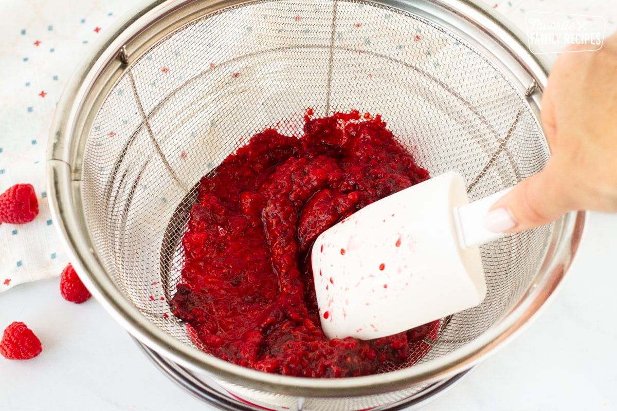 Spatula straining raspberry pulp and seeds for Raspberry Sauce.