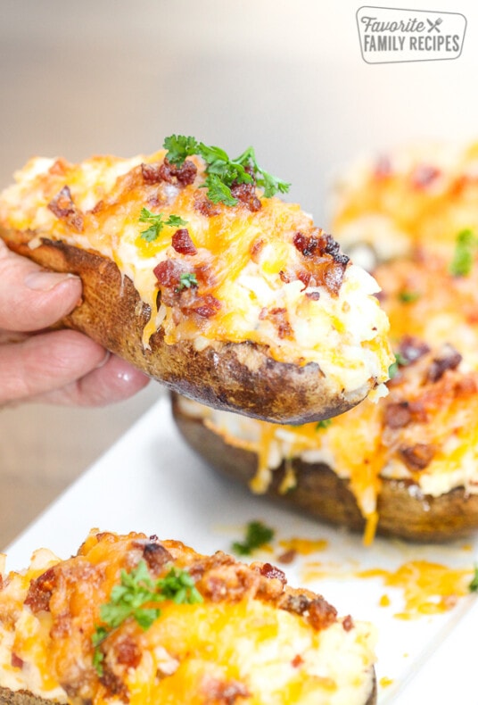 Twice baked potato being pulled up from a platter to show melted cheese and bacon.