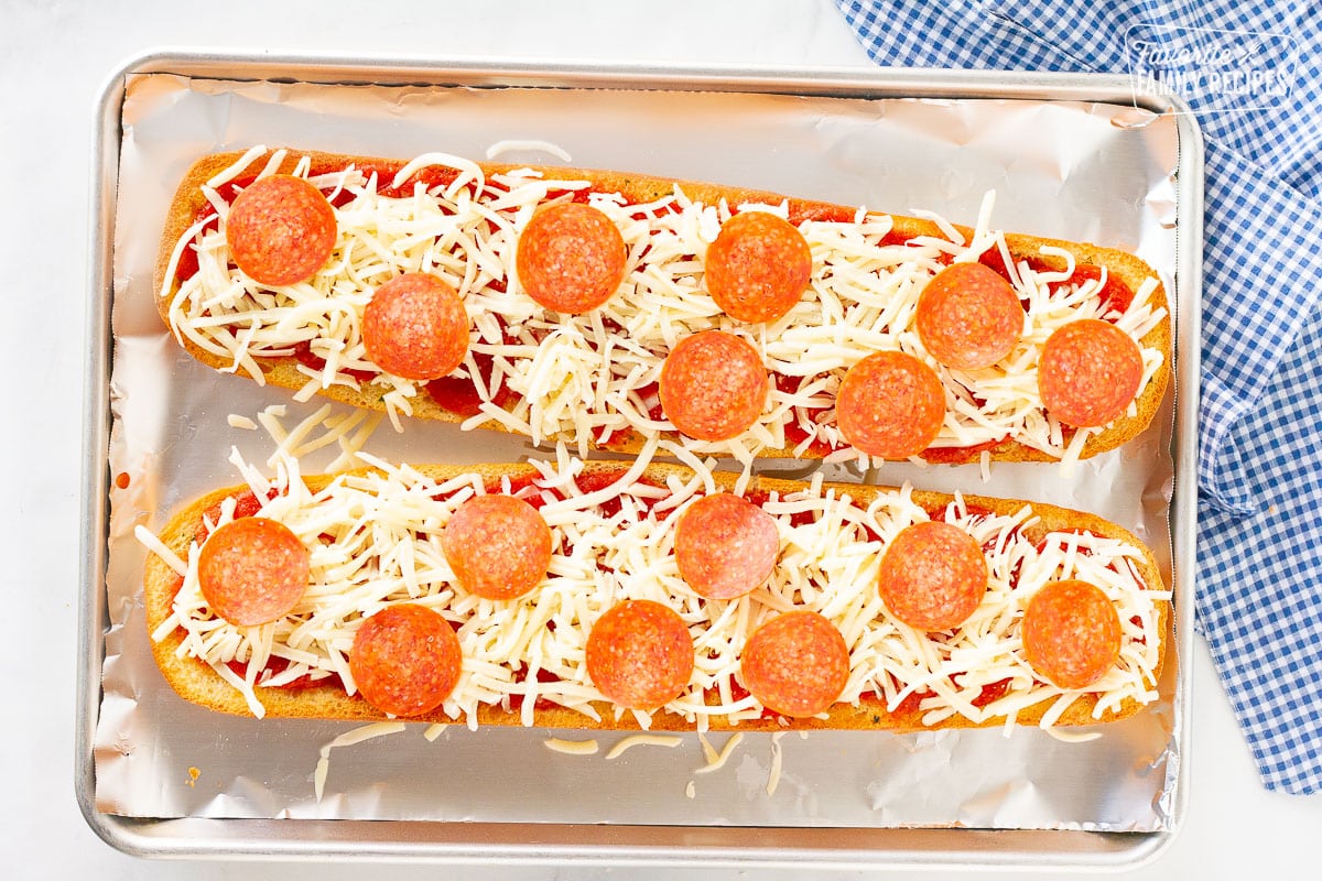 Two unbaked halves of French Bread Pizza on a cookie sheet covered in foil.