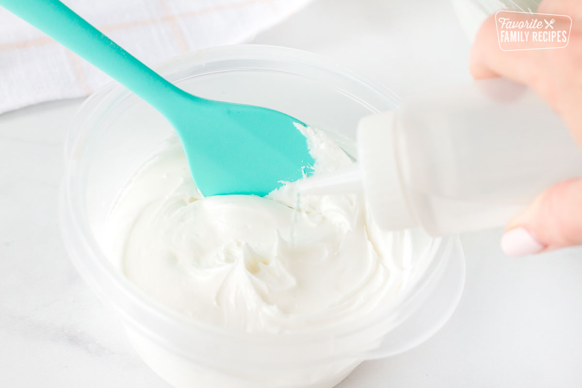Hand squeezing a bottle of water into a bowl of thick Royal Icing.