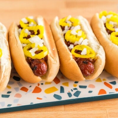 Four hot dogs in buns on a plate topped with onions and banana peppers