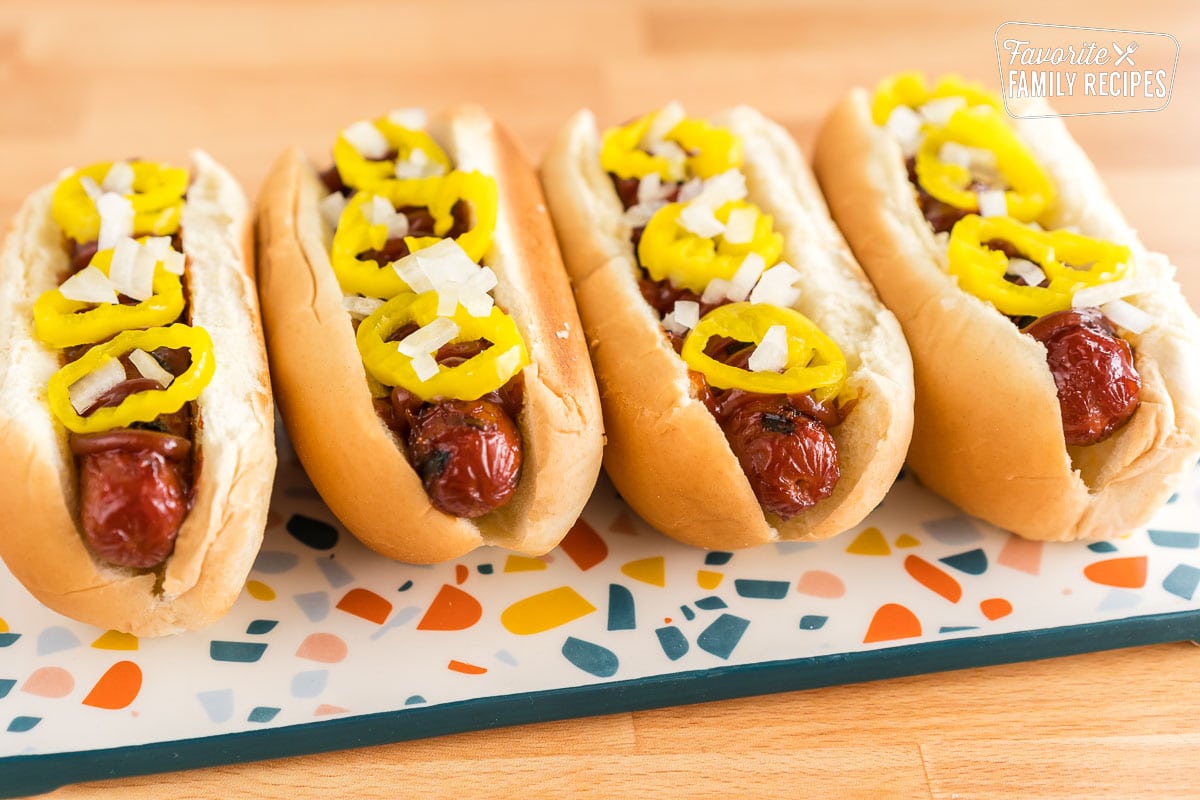Four hot dogs in buns on a plate topped with onions and banana peppers