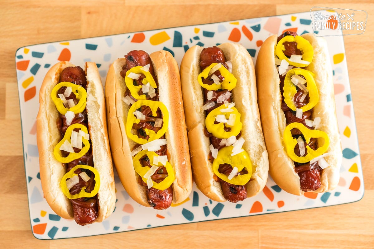 Four hot dogs in buns on a plate topped with onions and banana peppers