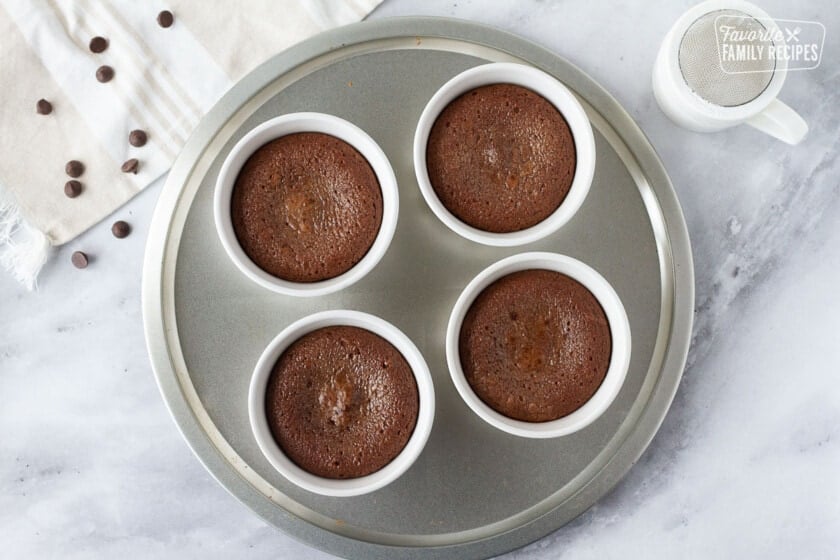 Four ramekins on a round pan with baked Carnival Cruise Melting Chocolate Cake. Powdered sugar on the side.