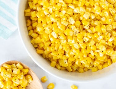 Bowl of Cooked frozen corn next to a wooden spoon of corn.