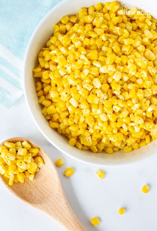 Bowl of Cooked frozen corn next to a wooden spoon of corn.