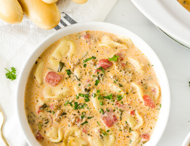 Bowl of Creamy Tortellini Soup next to a slow cooker and bread sticks.