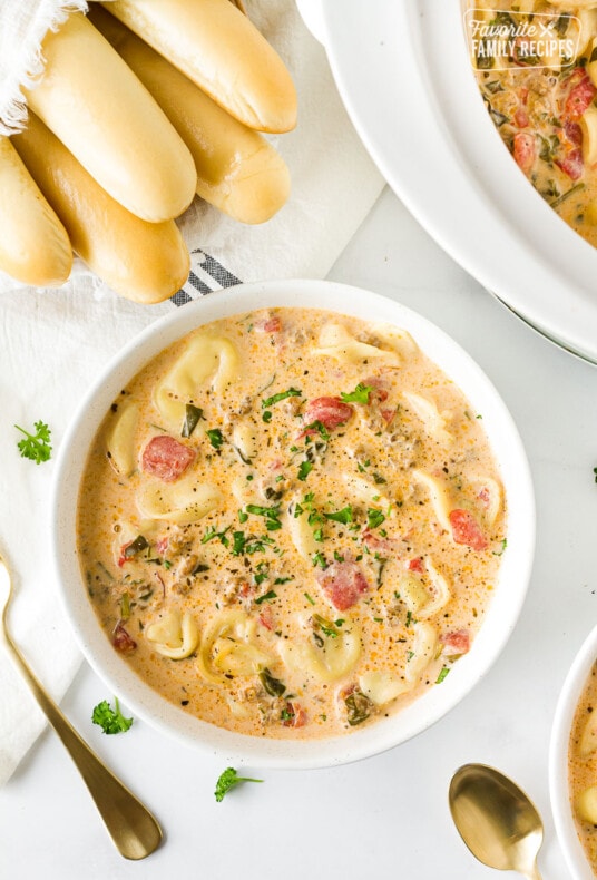 Bowl of Creamy Tortellini Soup next to a slow cooker and bread sticks.