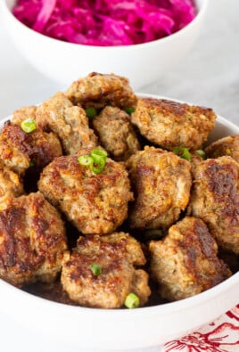 Bowl of Frikadeller (Danish Meatballs) garnished with green onions. Red cabbage and gravy on the side.