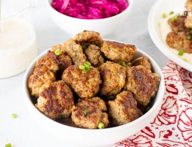 Bowl of Frikadeller (Danish Meatballs) garnished with green onions. Red cabbage and gravy on the side.