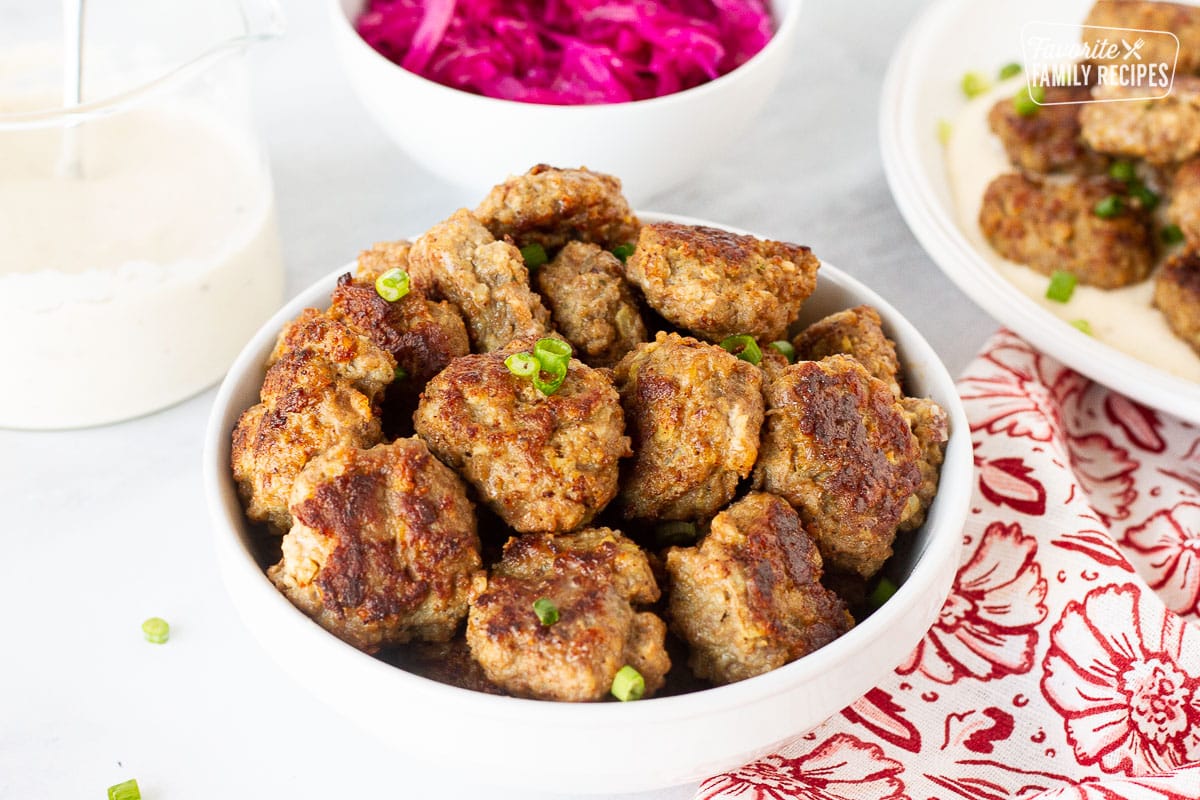 Bowl of Frikadeller (Danish Meatballs) garnished with green onions. Red cabbage and gravy on the side.