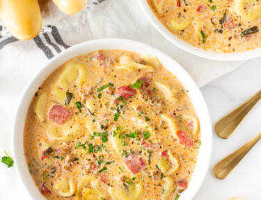 Two bowls of Creamy Tortellini Soup with breadsticks.