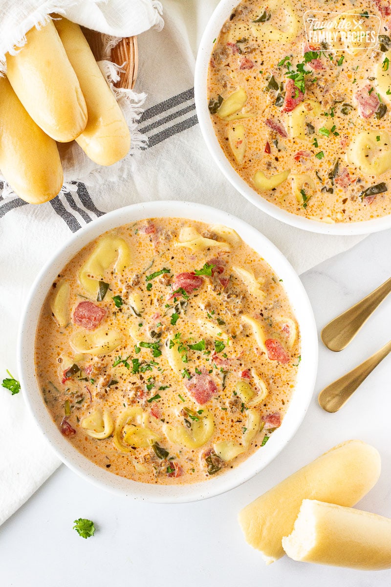 Two bowls of Creamy Tortellini Soup with breadsticks.