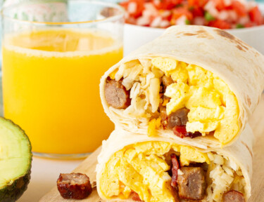 A breakfast burrito cut in half and stacked next to a glass of orange juice