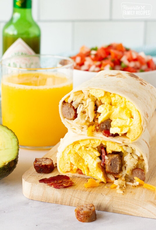 A breakfast burrito cut in half and stacked next to a glass of orange juice