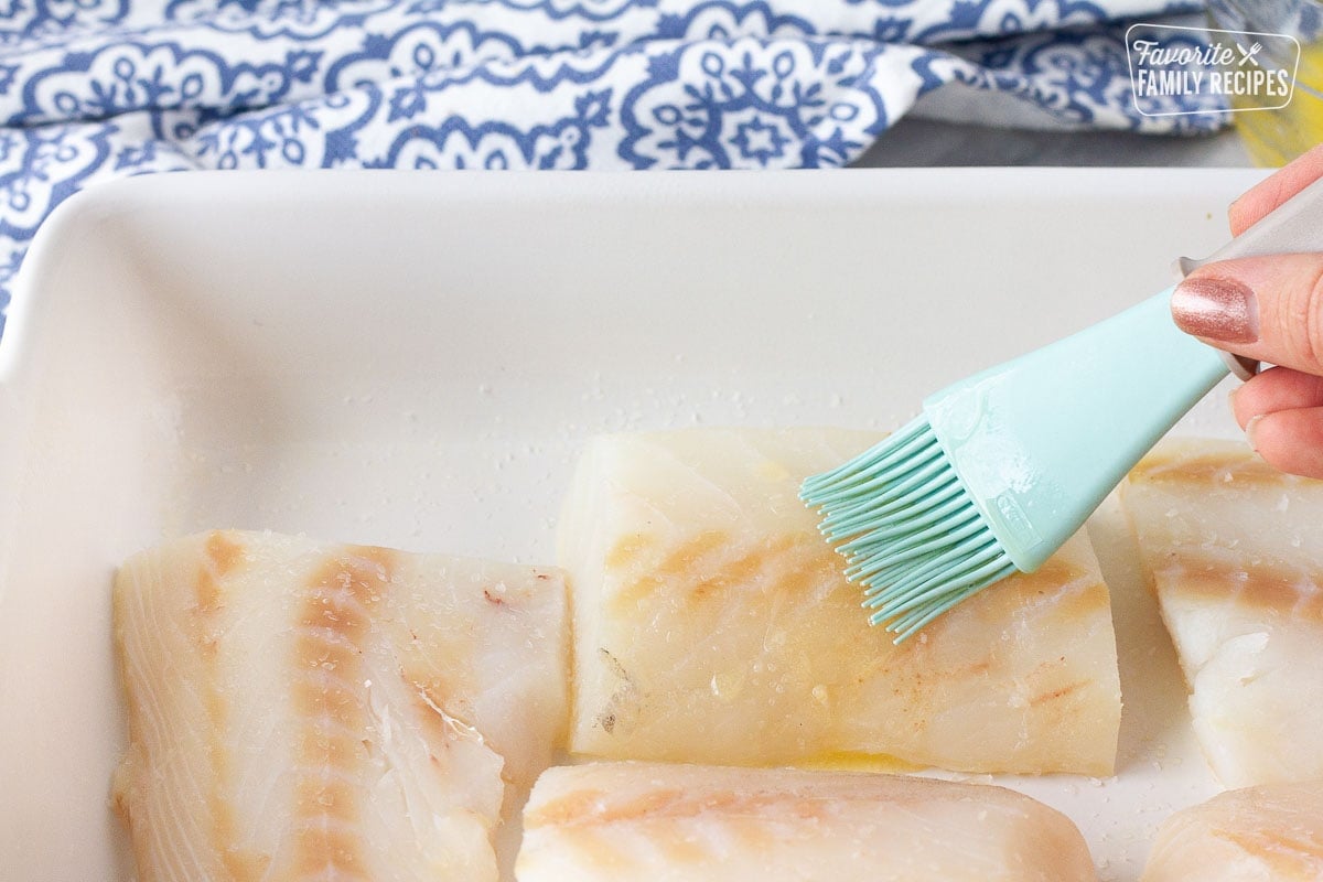 Hand brushing butter on a fillet of cod for Baked Cod in Cream Sauce.