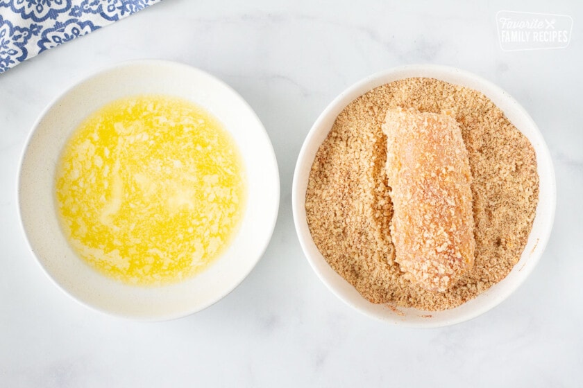 Bowl of melted butter and a bowl of panko mixture with a chicken breast for Chicken Cordon Bleu.