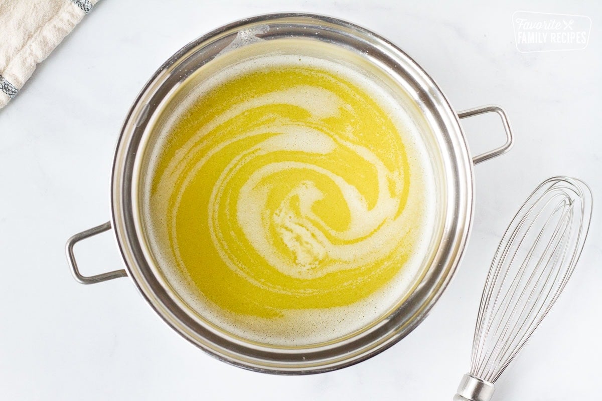 Pot of butter and broth swirling next to a whisk for Chicken Cordon Bleu Sauce.