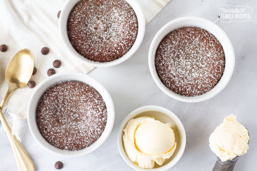 Three ramekins of Carnival Cruise Melting Chocolate Cake dusted with powdered sugar. Vanilla ice cream on the side.