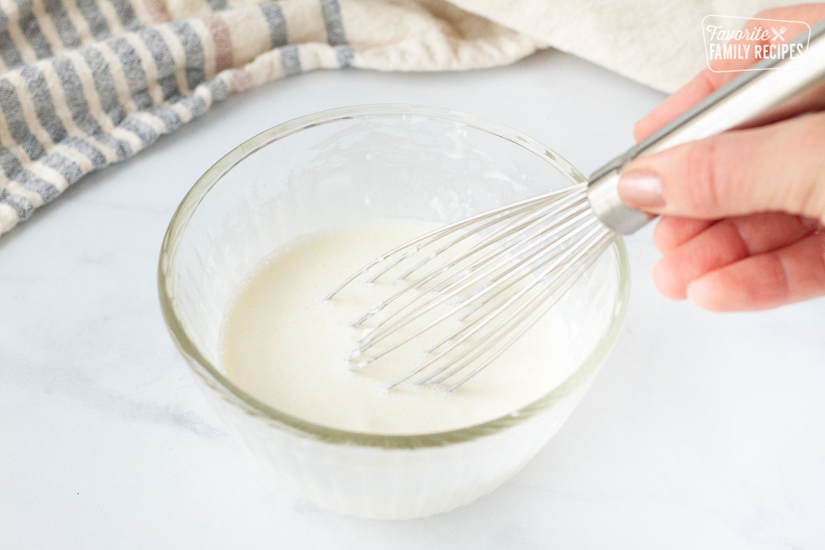 Bowl of cream and corn starch mixing with a whisk to make Chicken Cordon Bleu Sauce.