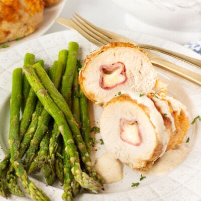 Chicken Cordon Bleu cut in half on a plate with roasted asparagus.