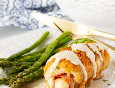 Plate of Chicken Cordon Bleu covered with sauce and a side of asparagus.
