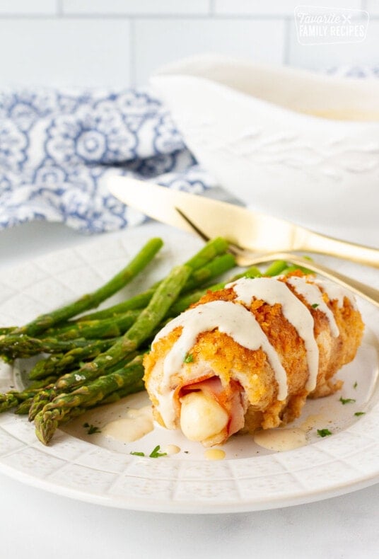 Plate of Chicken Cordon Bleu covered with sauce and a side of asparagus.