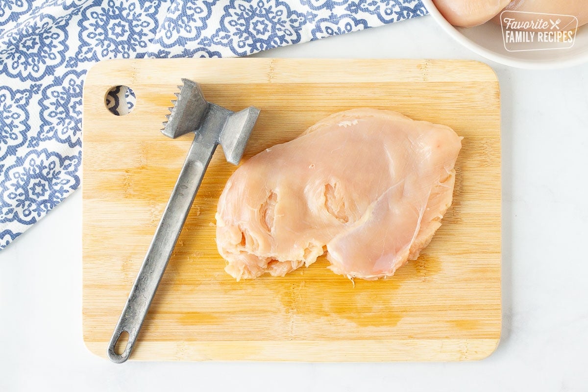 Cutting board a flattened Chicken Breast with a metal mallet for Chicken Cordon Bleu.
