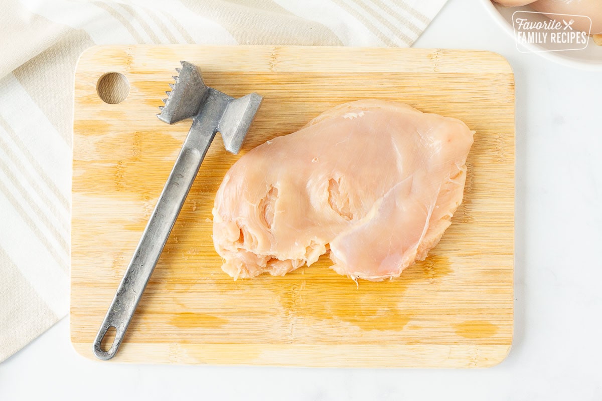 Chicken breast flattened next to a metal mallet on a cutting board for Instant Pot Chicken Cordon Bleu.