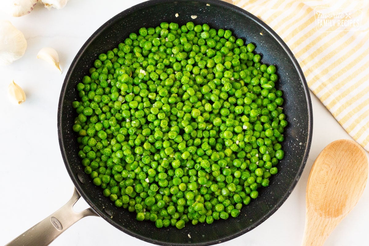Frozen Peas in a skillet next to a wooden spoon.