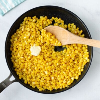 Skillet with wooden spoon and butter cooking Frozen Corn.