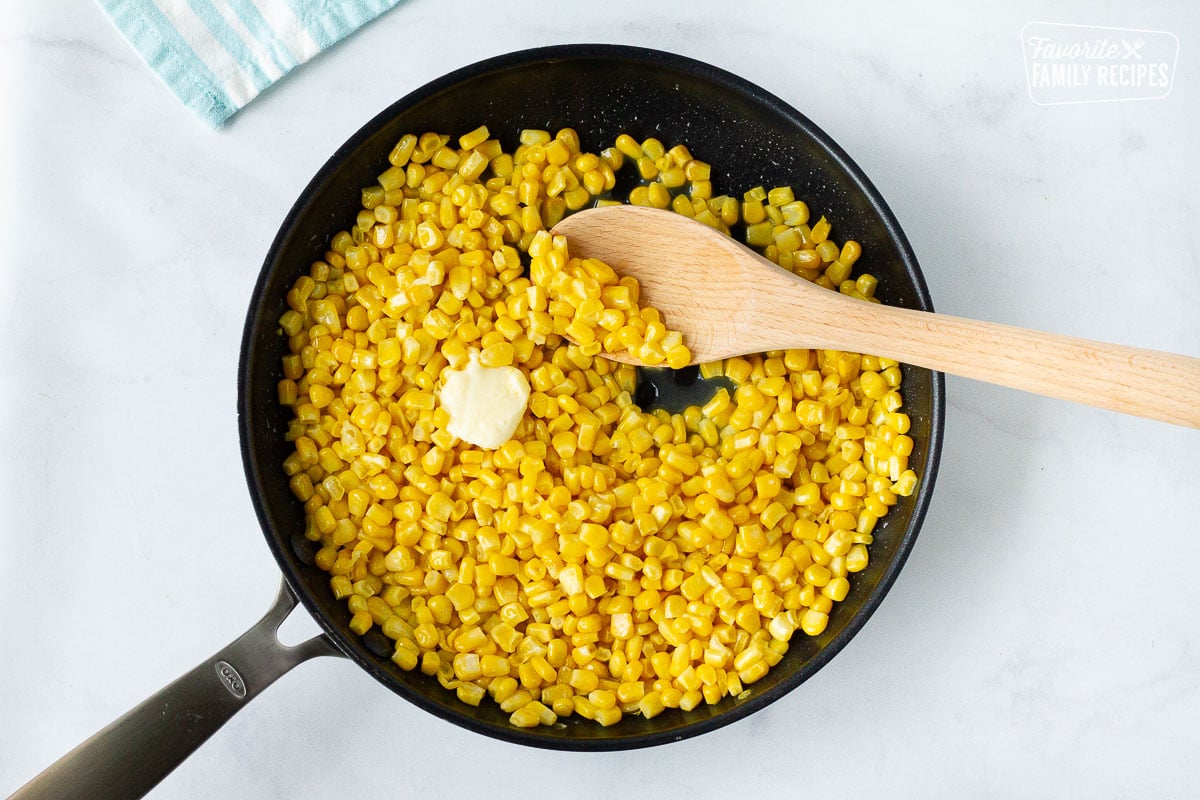 Skillet with wooden spoon and butter cooking Frozen Corn.